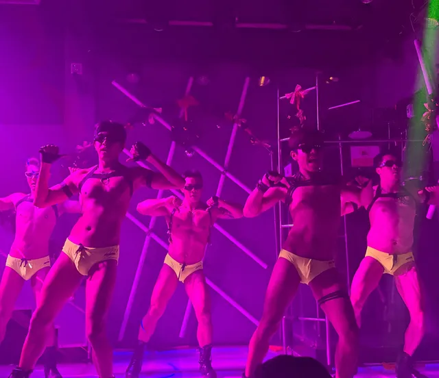 Male dancers performing in formation under magenta stage lighting