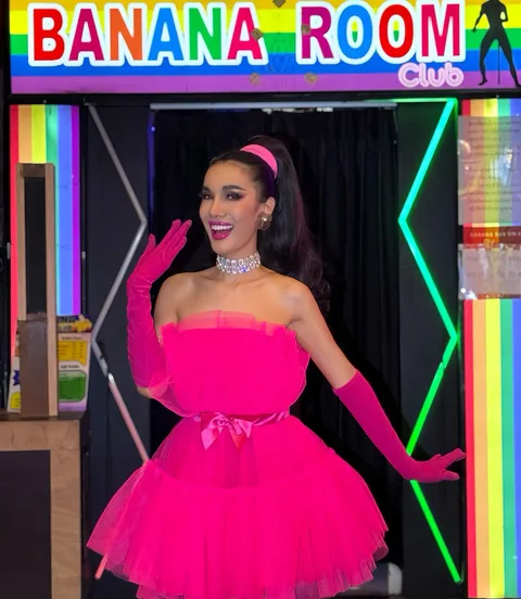 Cabaret performer in a pink dress beneath the rainbow Banana Room Club sign