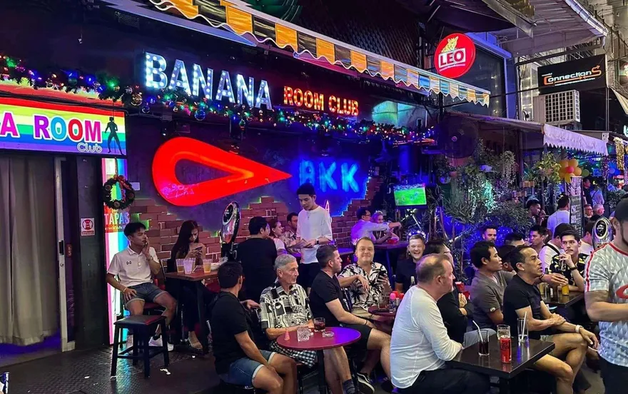 The outdoor terrace at night under the Banana Room Club neon sign, full of guests