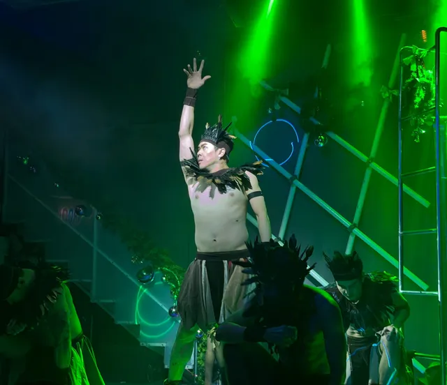 Solo performer under a green spotlight with one arm raised
